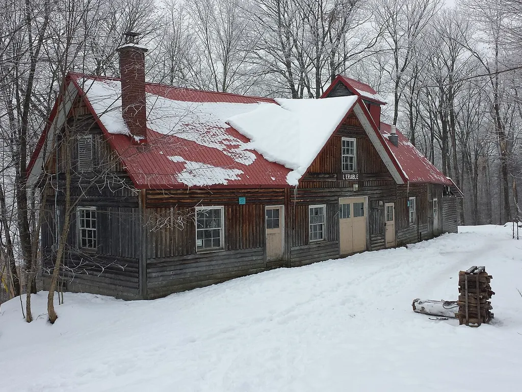 Une cabane à sucre en bois au toit rouge dans une érablière enneigée à Duchesnay, Quebec