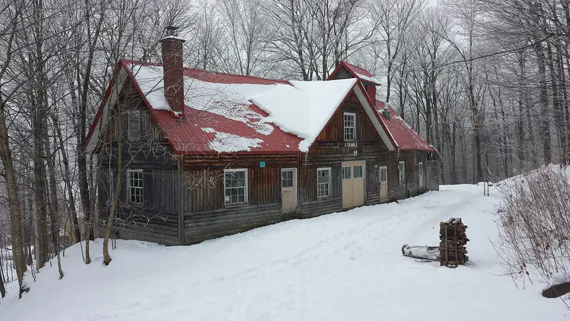 Une cabane à sucre en bois au toit rouge dans une érablière enneigée à Duchesnay, Quebec
