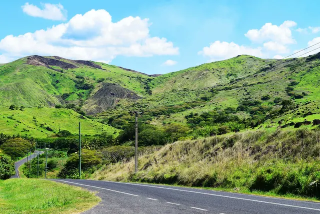 A country road winding below green hills under a blue sky in Fiji