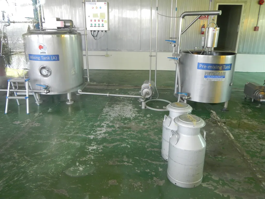 Two stainless steel milk tanks labelled Mixing Tank and Pre-mixing Tank, with two aluminium milk cans on a green dairy-plant floor