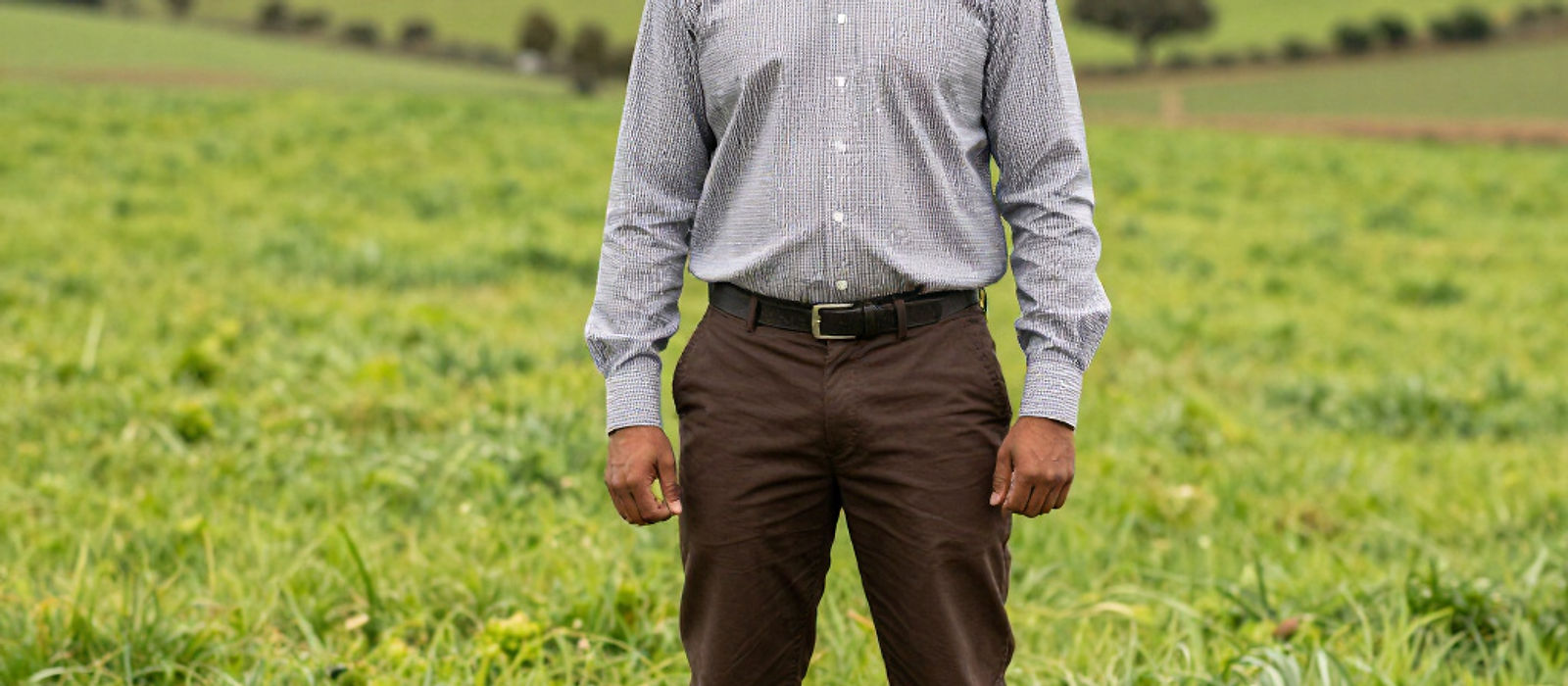 A farmer standing in a green field with rolling hills behind him